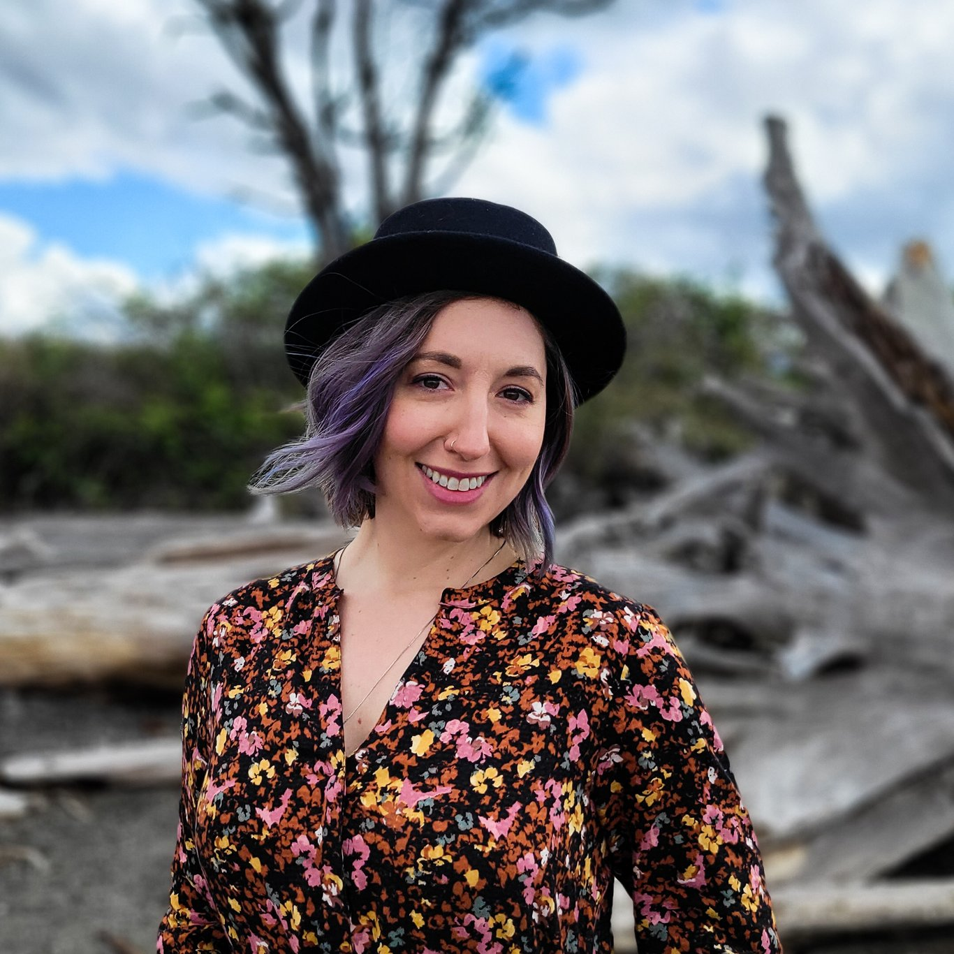 A close-up headshot of Elizabeth Jenkins along the Puget Sound. She is smiling while wearing a floral blouse and black hat.